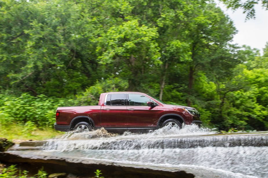 A red Honda Ridgeline pickup truck, assembled in the U.S.A. fords a stream.