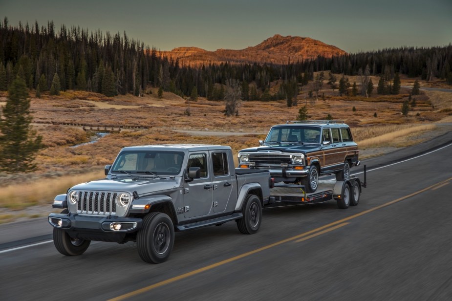 A silver Jeep Gladiator diesel pickup truck tows a vintage Wagoneer SUV, trees and mountains visible in the background.