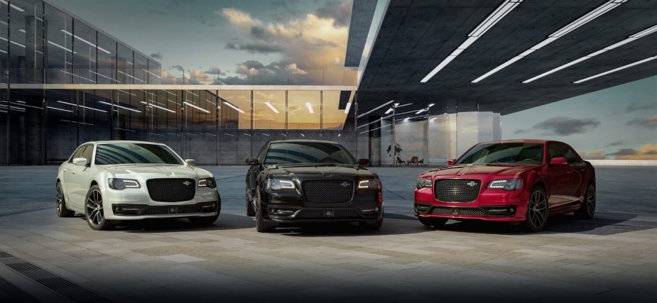 A white, black, and red Chrysler 300 sedan lined up in front of a glass building reflecting the sunset.