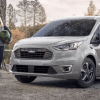 A gray 2023 Ford Transit Connect compact panel van commercial vehicle parked near a forest river during a camping trip