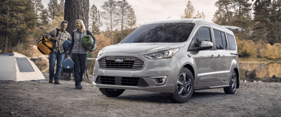 A gray 2023 Ford Transit Connect compact panel van commercial vehicle parked near a forest river during a camping trip