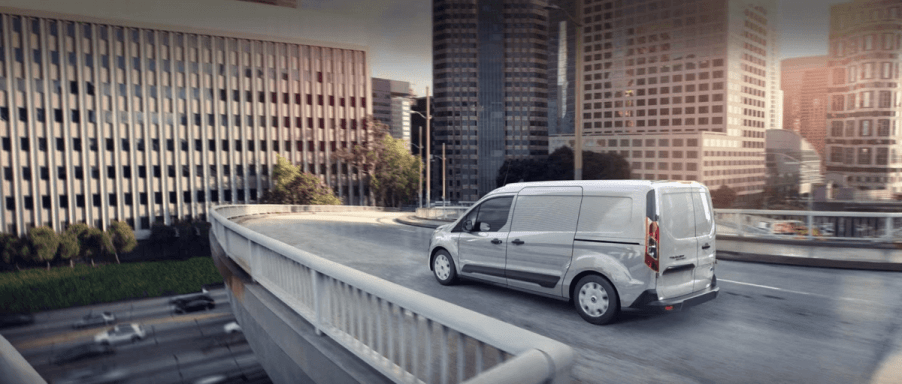 A white 2023 Ford Transit Connect compact panel van commercial vehicle driving on a city highway overpass