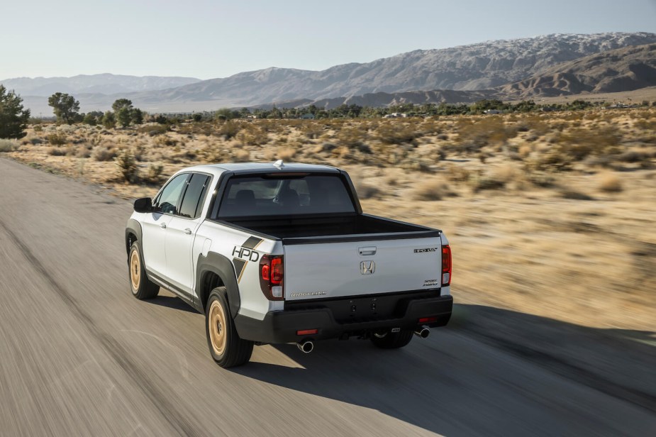 A white Honda Ridgeline compact pickup truck driving away, on a road through the desert.