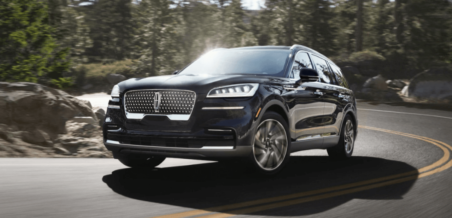 A 2023 Lincoln Aviator midsize luxury SUV model driving on a forest highway road