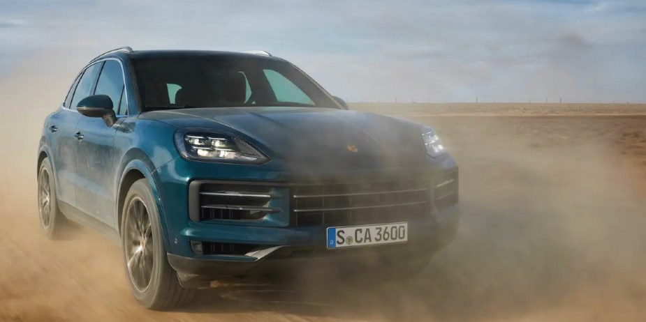 A blue 2023 Porsche Cayenne luxury SUV is driving on a dirt road. 