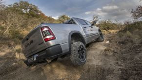 A gray Ram 1500 Rebel's suspension flexes as it navigates an off-road obstacle.