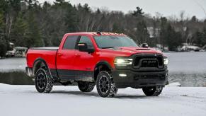 A red 2023 Ram 2500 Heavy Duty Rebel pickup truck model parked in the snow near a forest and frozen lake