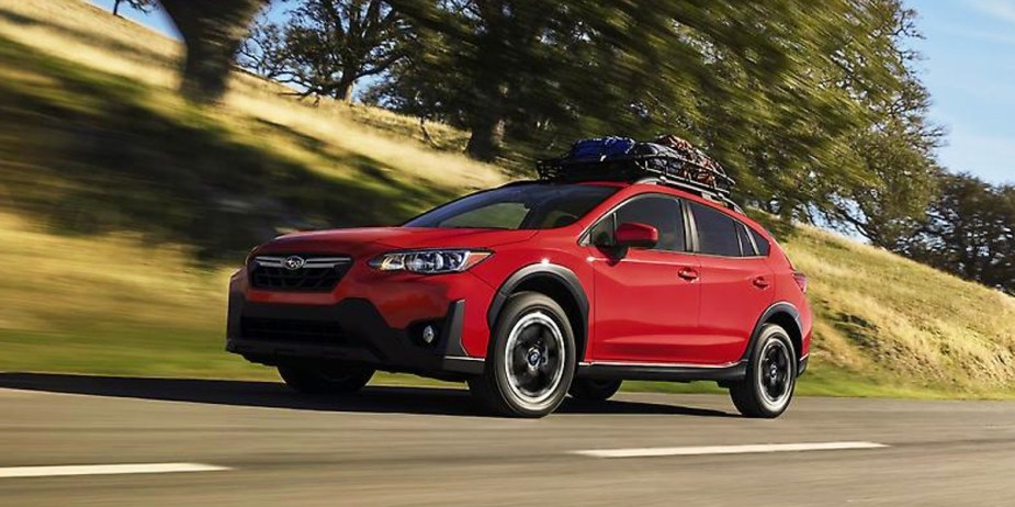 A red 2023 Subaru Crosstrek subcompact SUV is driving on the road. 