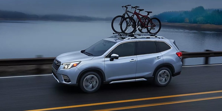 A blue 2023 Subaru Forester small SUV is driving on the road.