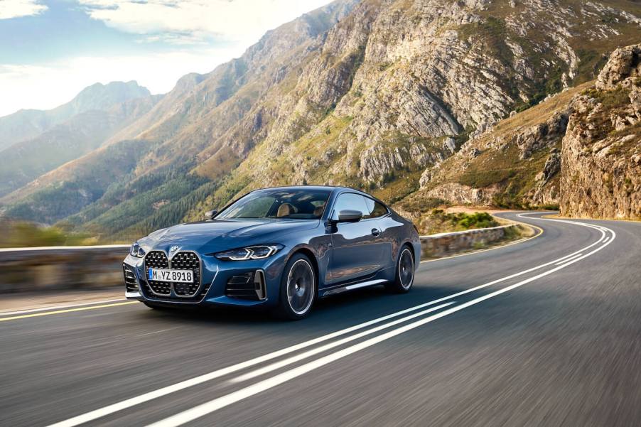 A blue 2024 BMW 4 Series driving down a winding road with cliffs in the background.