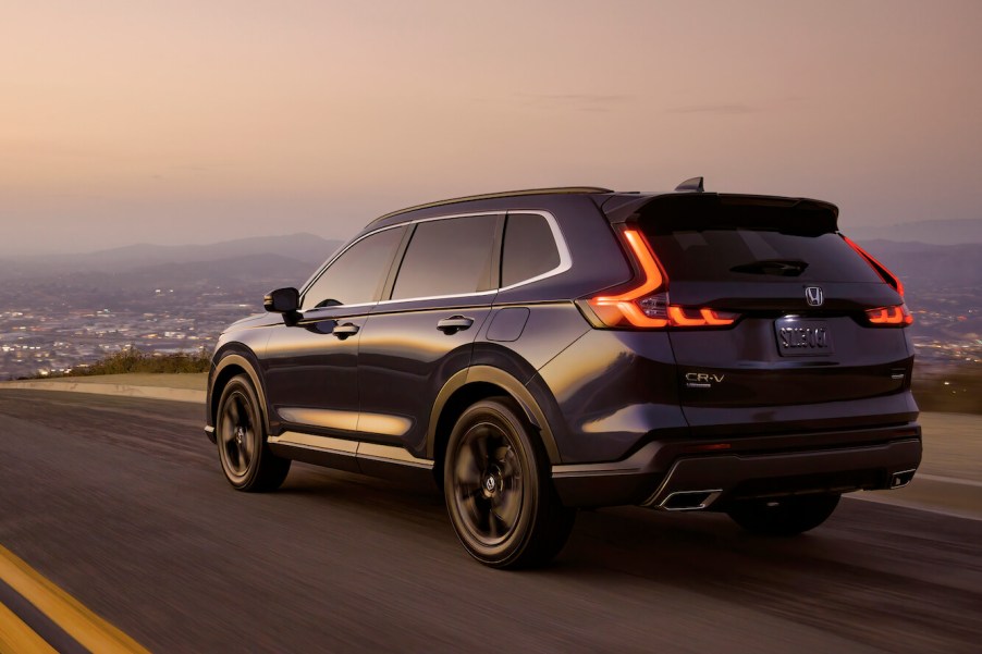 A blue 2024 Honda CR-V Sport Touring, powered by another edition of the classic CR-V engine, driving on the road at sunset.