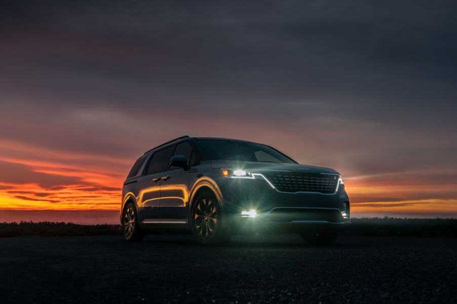 A 2024 Kia Carnival minivan/MPV model parked in the dark at sunset with its headlights on