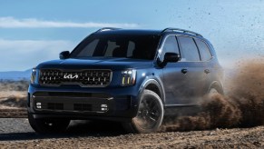 A blue 2024 Kia Telluride midsize SUV is driving off-road.