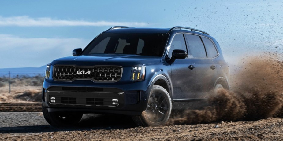 A blue 2024 Kia Telluride midsize SUV is driving off-road. 