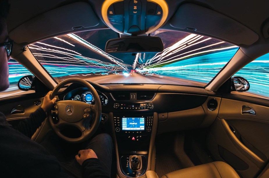 Time-lapse photo of man driving his car, the headlights of other vehicles streaking by outside his windshield.