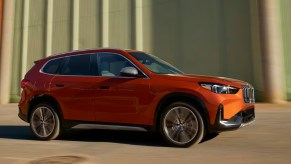 An Orange 2023 BMW X1 is driving.