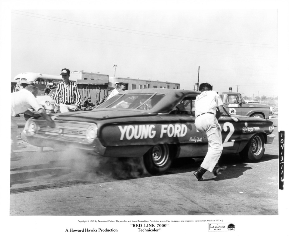 A race car takes off while its pit crew pushes in still from black and white car movie "Red Line 7000"