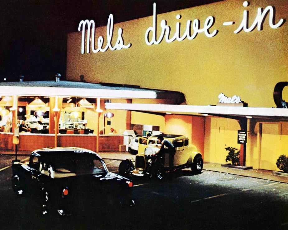 George Lucas directs two cars during a night-time scene outside Mel's Drive-In in San Francisco, California, while filming 'American Graffiti', 1973.