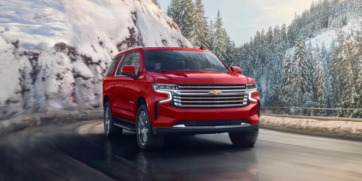 A red 2023 Chevrolet Suburban full-size SUV is driving on the road.