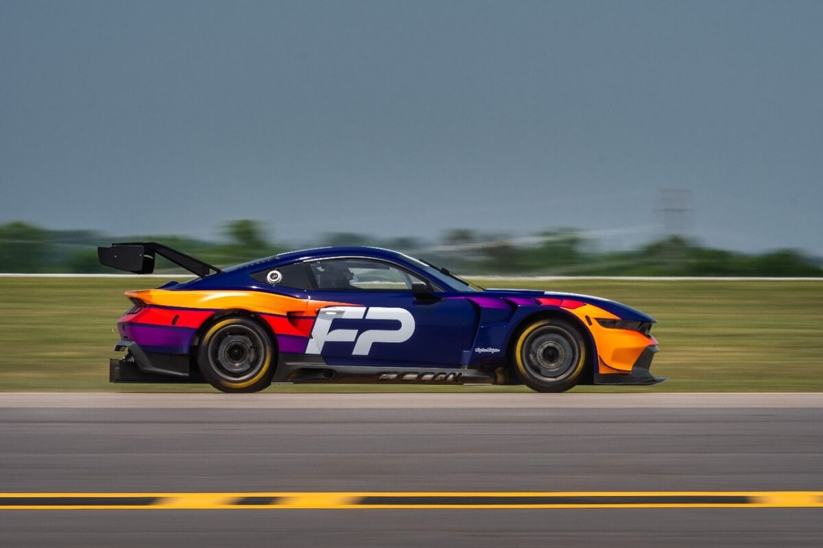 A brightly-colored race car drives on a track in preparation for Le Mans.