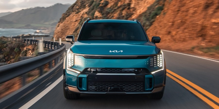 A blue 2024 Kia EV9 fully-electric SUV is driving on the road.