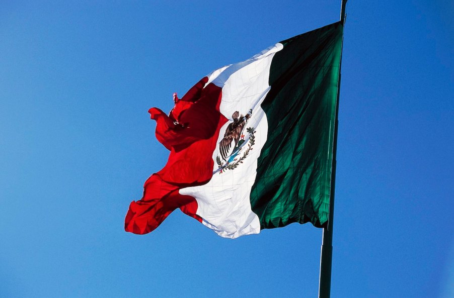 The Mexican national flag flying in front of a blue sky.