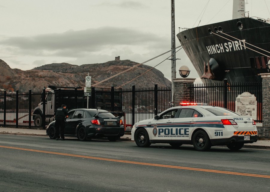 A Black Subaru car being pulled over and given a speeding ticket by a police officer