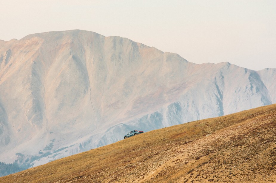 A Rivian pickup truck descending a ridge line, a mountain visible in the background.