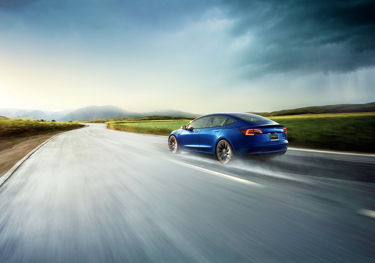 A blue Tesla Model 3 electric car uses its AWD to grip a wet road. 