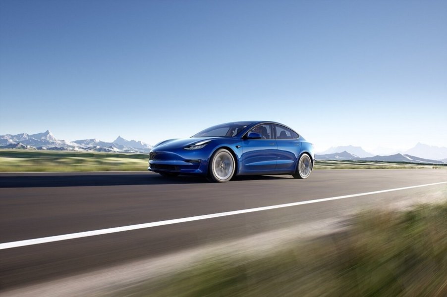 A blue Tesla Model 3 drives down a mountain road with AWD grip.