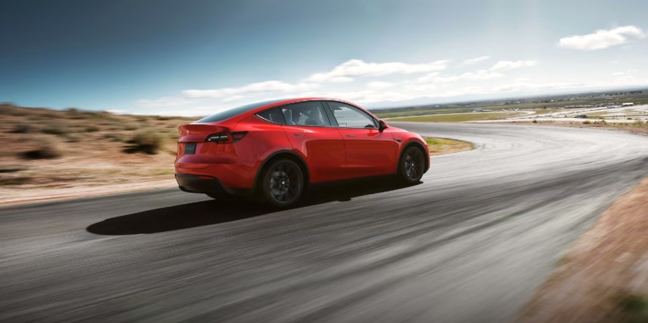 A red 2023 Tesla Model Y small electric SUV is driving on the road. 