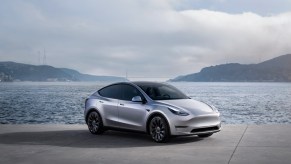 A gray 2023 Tesla Model Y small electric SUV is parked near water.