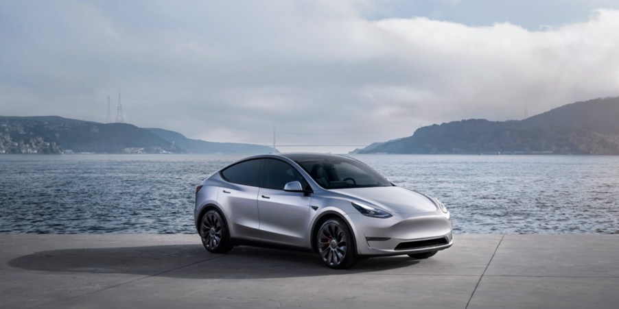 A gray 2023 Tesla Model Y small electric SUV is parked near water.