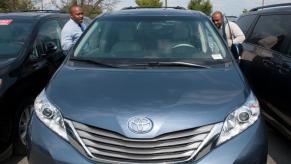 Two men looking at a used Toyota Sienna in a car dealership lot.