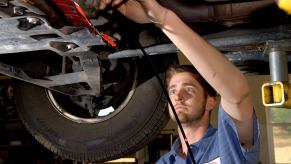 A man who is working as a mechanic or automotive service technician changes the oil of a car on a lift.