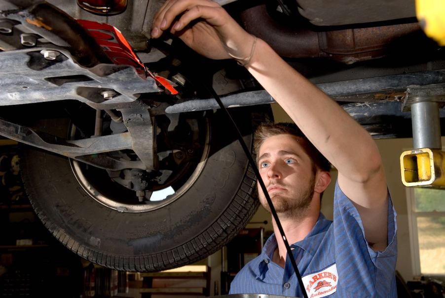 A man who is working as a mechanic or automotive service technician changes the oil of a car on a lift.