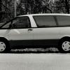 A black and white photo of a Toyota Previa minivan model in side profile parked near a wooden fence