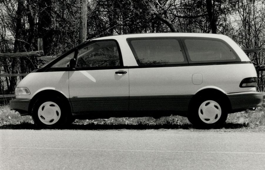 A black and white photo of a Toyota Previa minivan model in side profile parked near a wooden fence