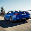 A BMW M4 Competition Convertible model driving on a highway past forest trees with xDrive