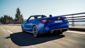 A BMW M4 Competition Convertible model driving on a highway past forest trees with xDrive