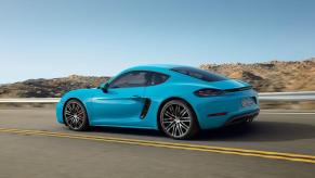 A blue Porsche 718 Cayman drives on a roadway.