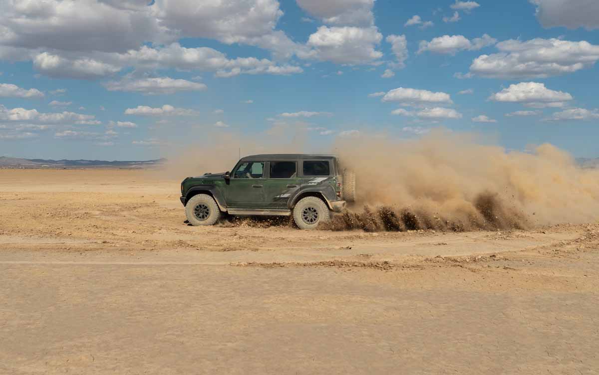 Ford Bronco Raptor throwing dirt high in the air while spinning tires in the desert.