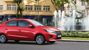 A 2023 Mitsubishi Mirage G4 subcompact sedan model driving past a park water fountain