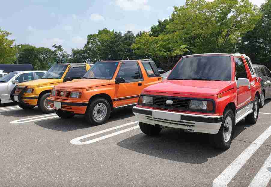 Three Geo Trackers parked next to each other all in different colors; yellow, orange, and red.