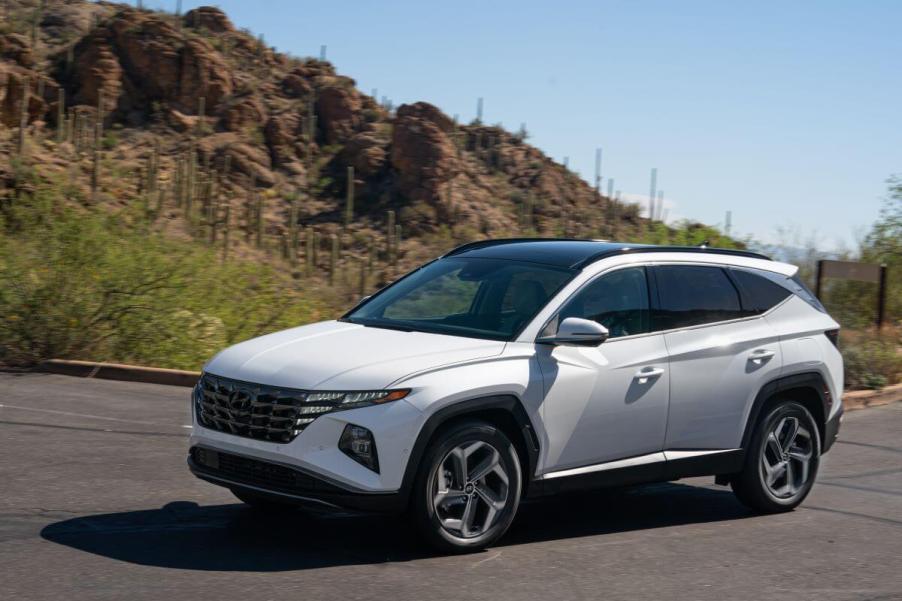 A 2023 Hyundai Tucson Hybrid compact SUV model in white driving in a desert environment with cacti