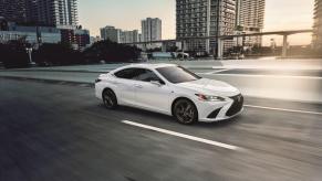 A white 2023 Lexus ES 350 midsize executive car/luxury sedan model driving past city skyscrapers