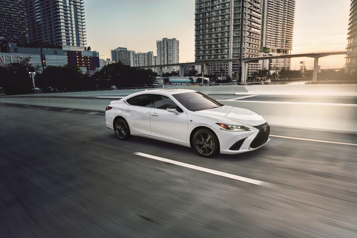 A white 2023 Lexus ES 350 midsize executive car/luxury sedan model driving past city skyscrapers