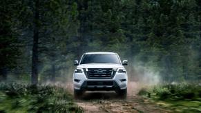 A 2023 Nissan Armada full-size SUV model driving on a trail within a deep green forest of evergreens