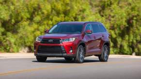 A red 2018 Toyota Highlander travels on a highway alongside green shrubs