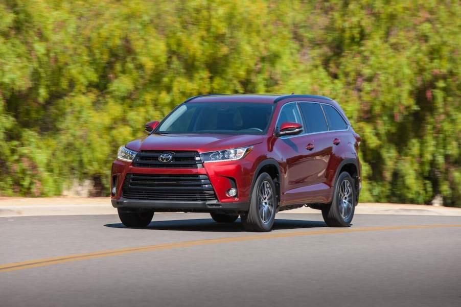 A red 2018 Toyota Highlander travels on a highway alongside green shrubs